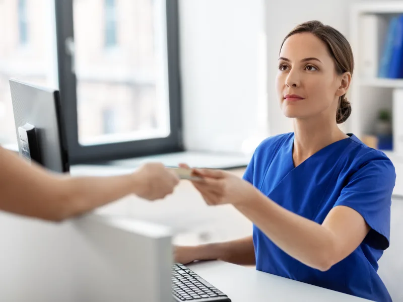 Patient handing an insurance card to a member of the practice team at the front desk