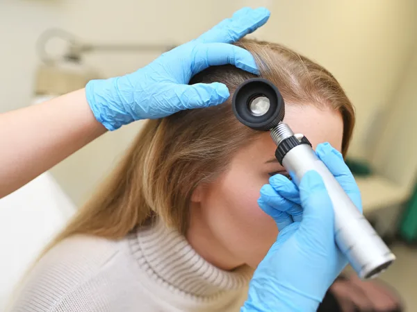Dermatologist examining a patient's scalp and hair with a dermatoscope