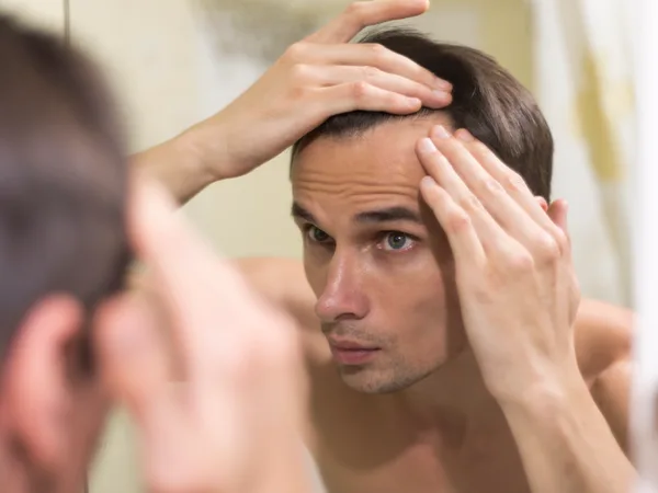 Man examining his thinning hairline in the mirror before PRP hair loss treatment