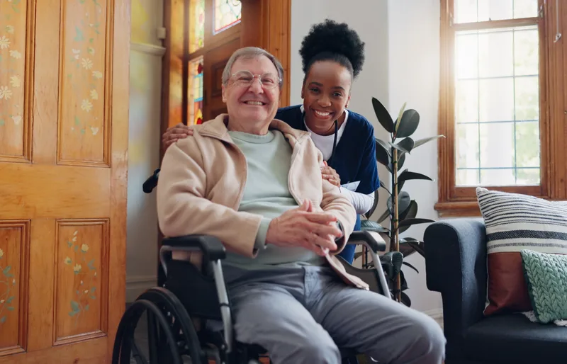 Caregiver supporting a smiling senior man in a wheelchair in a care home lounge