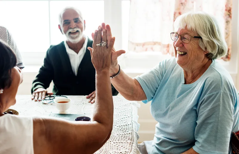 Seniors laughing and sharing a high five around the table in an assisted living community