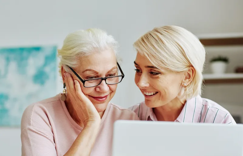 Adult daughter and her mother reviewing senior care options together on a laptop