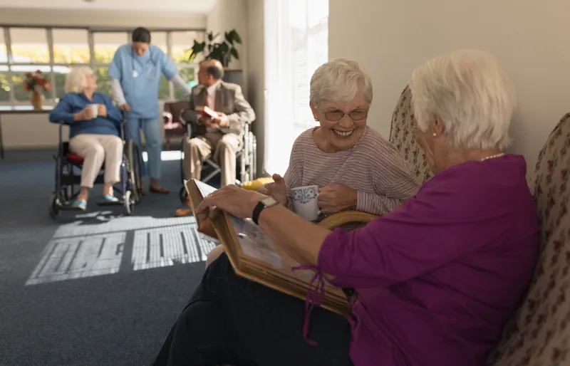 Two senior women sharing a photo album over coffee in a senior living community lounge