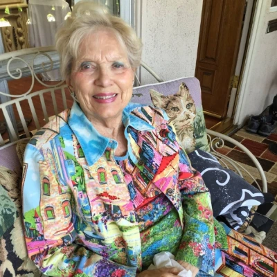 Smiling senior woman in a brightly patterned blouse seated in a sunlit garden room
