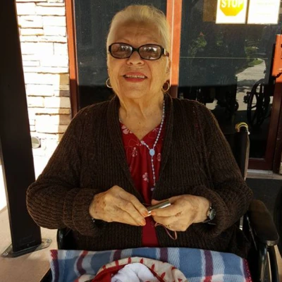 Senior woman crocheting in her wheelchair outdoors with a striped blanket across her lap