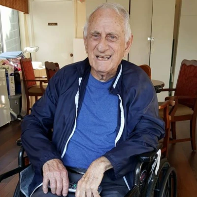 Senior man in a navy jacket smiling from his wheelchair in a care community lounge