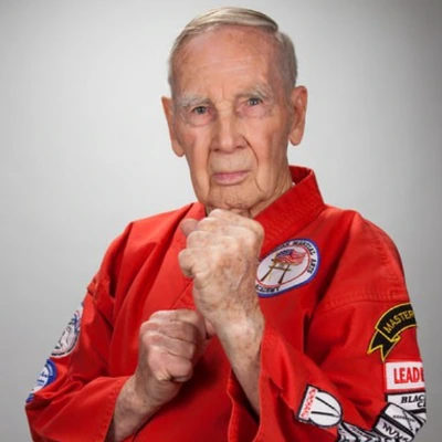 Senior man in a patch-covered red martial arts uniform holding a guard stance