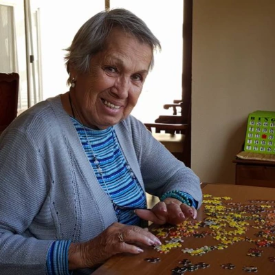 Senior woman looking up with a smile while piecing together a jigsaw puzzle at her dining table