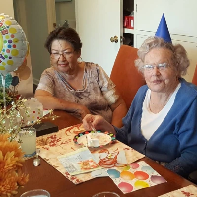 Two senior women celebrating a birthday, one in a party hat cutting the cake