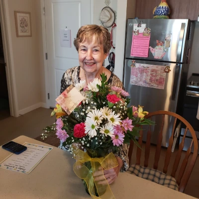 Senior woman in her kitchen holding a large bouquet of flowers with a gift card tucked inside