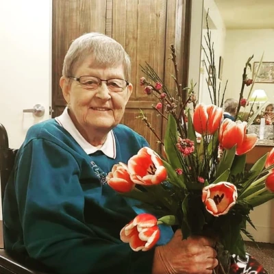 Senior woman in a green sweater smiling beside a vase of red tulips