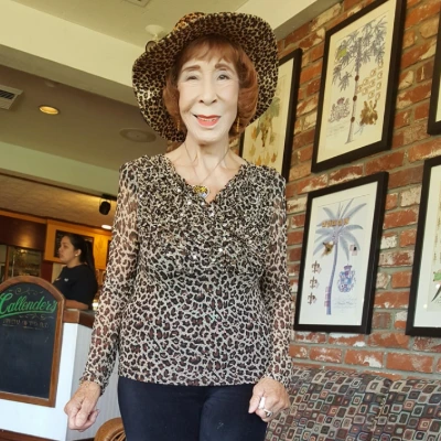 Senior woman in a leopard-print top and matching wide-brimmed hat standing in a restaurant