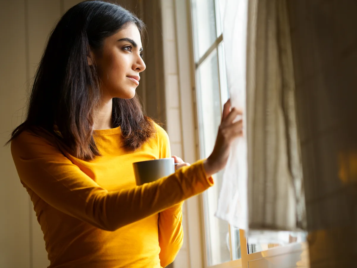 Woman pausing by a sunlit window with a cup of coffee, reflecting on a season of change