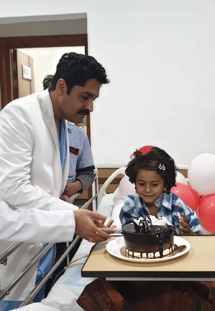 Dr. Kapoor cutting a celebration cake with a young patient on the ward